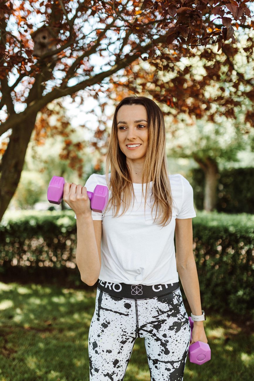 a smiling woman in activewear exercising using dumbbells