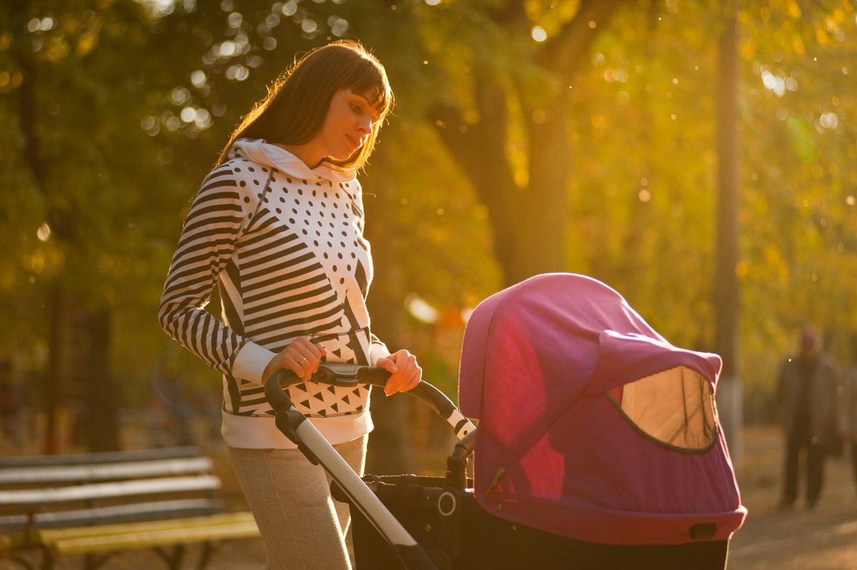 A mother walking with her baby in a stroller through a sunlit park, taking things one gentle step at a time postpartum